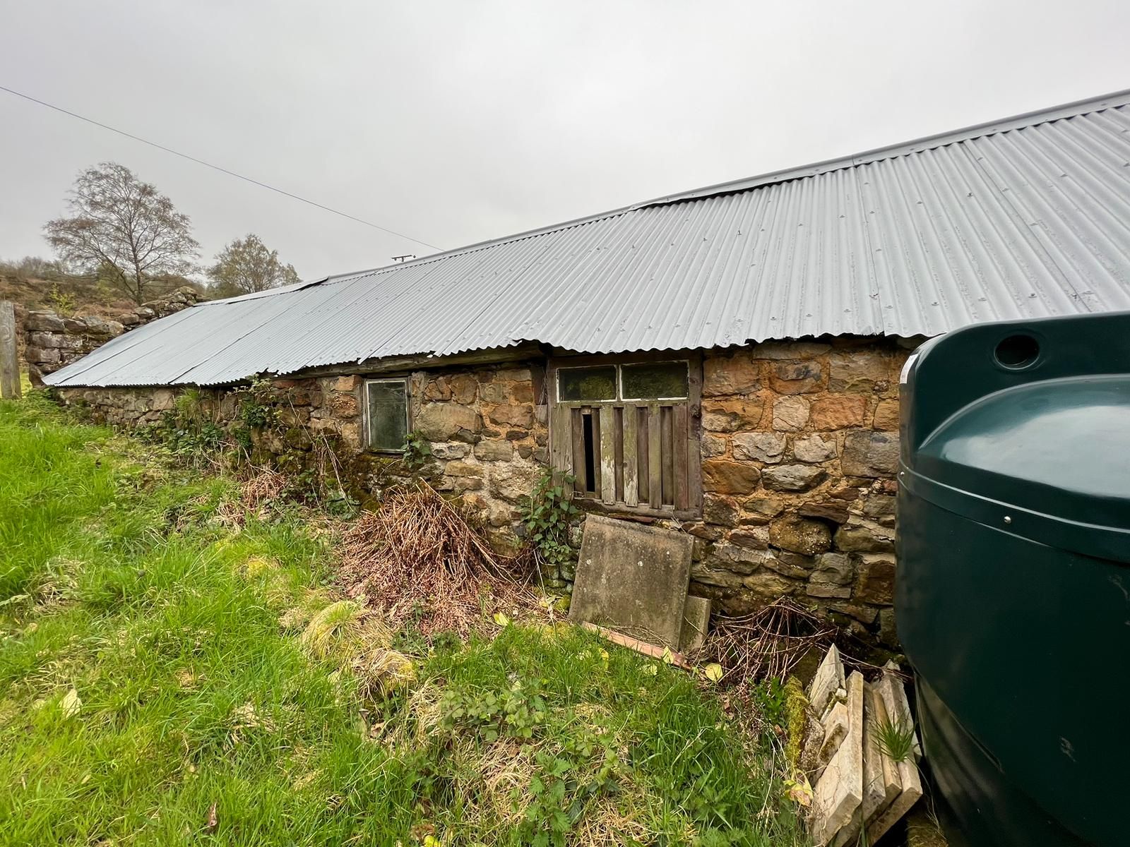 Old stone building with a corrugated metal roof and a green fuel tank in the foreground.