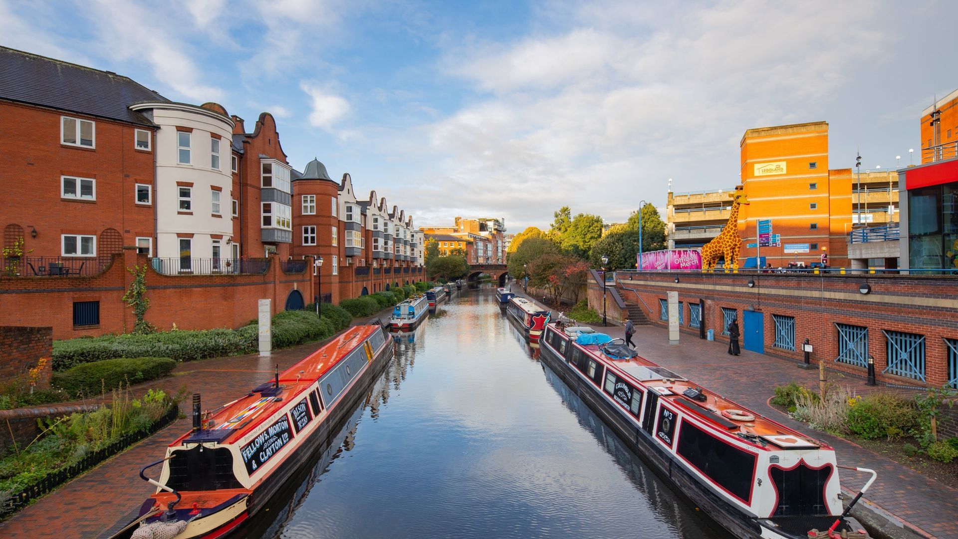 Canal with colorful narrowboats, brick buildings and blue sky in Birmingham, England.