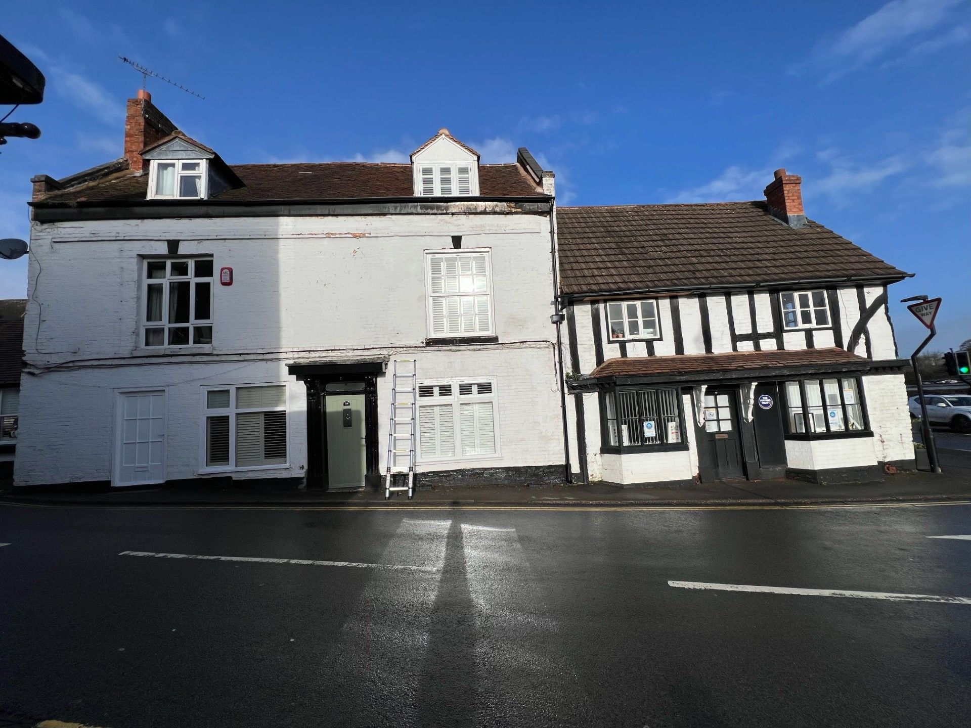Two-story building, white painted on the left, half-timbered on the right, on a street under a blue sky.