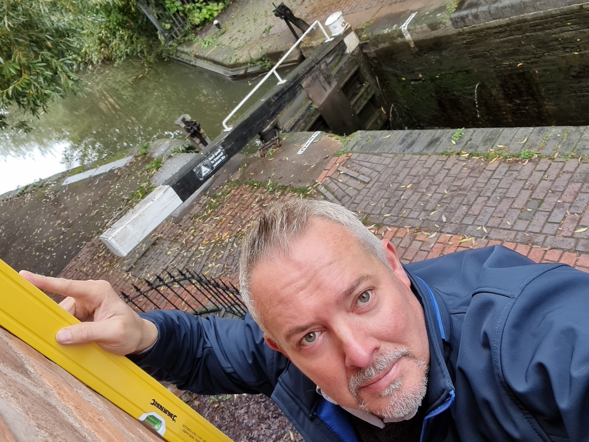 Man using level on brick wall near canal lock.