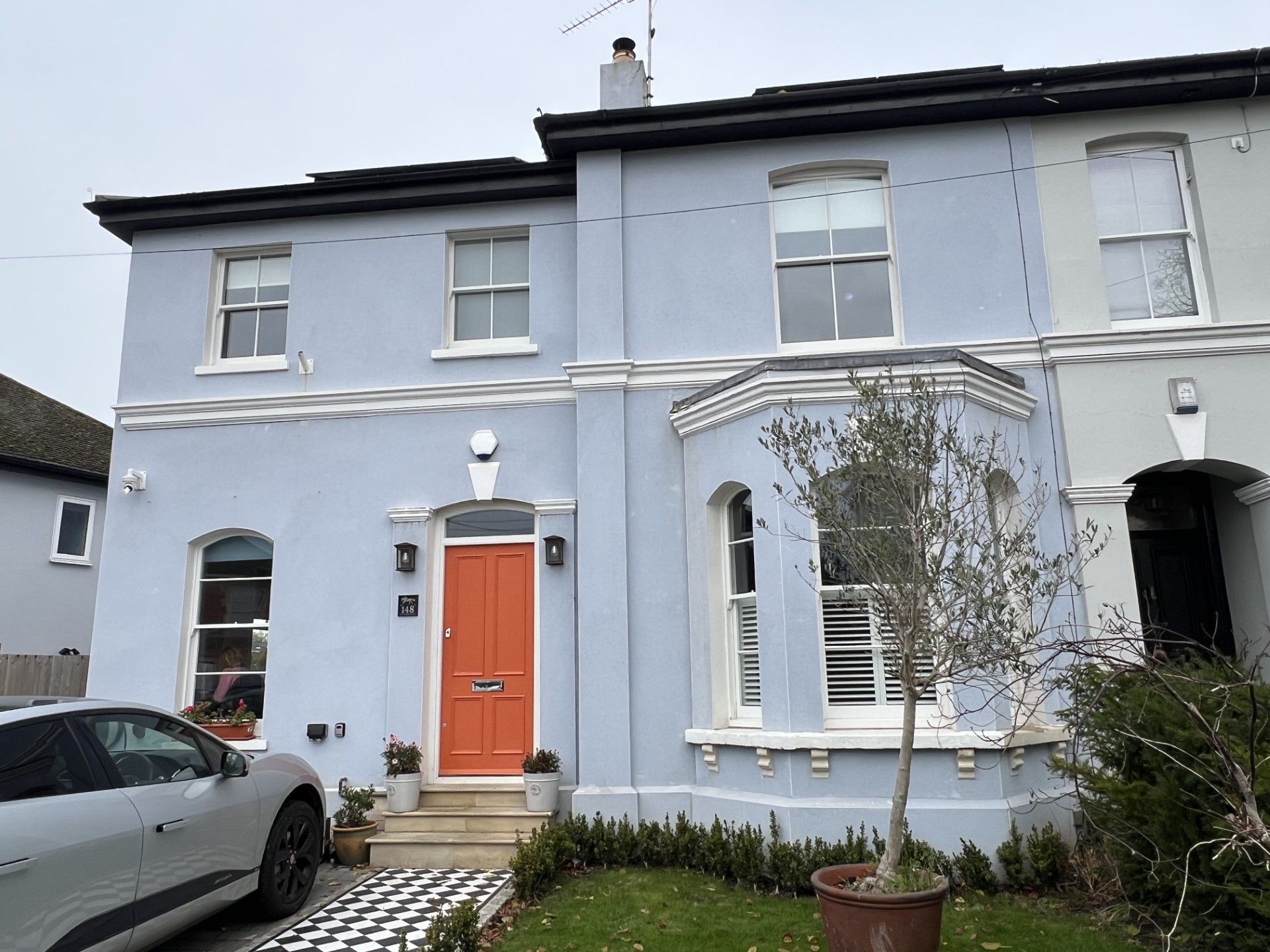 Blue painted house with an orange door, next to a car and other houses.