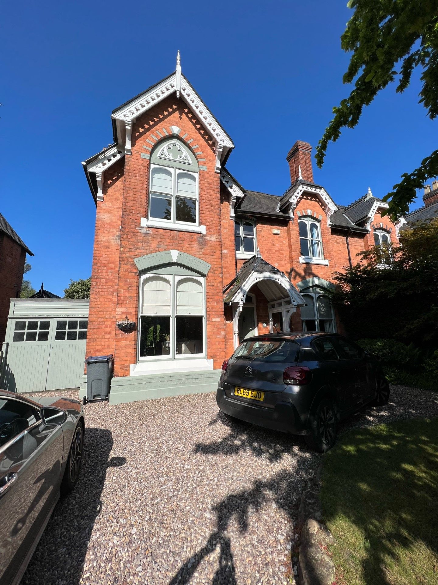 Red brick Victorian house with arched windows, car in the gravel driveway, sunny day.