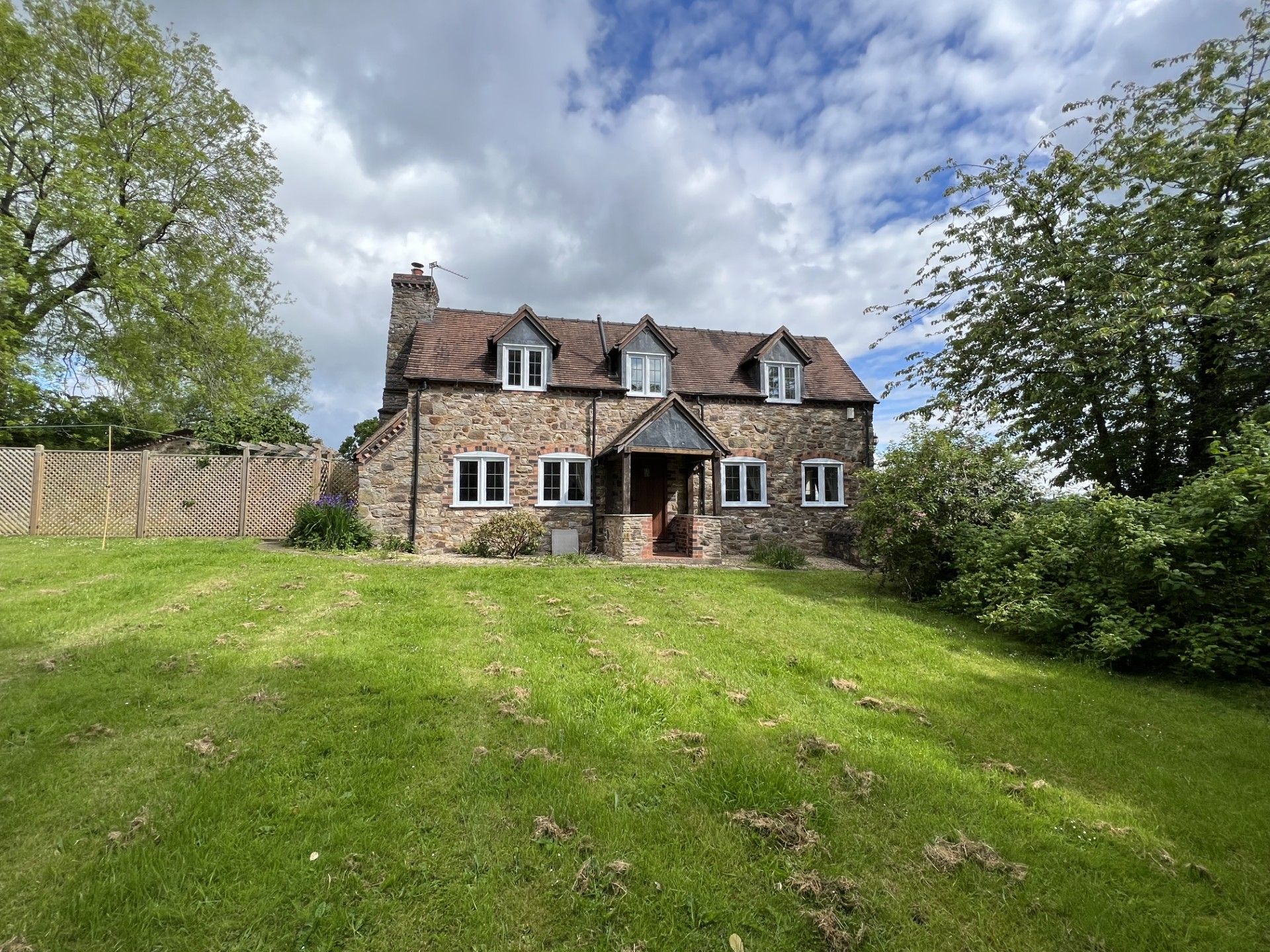 Stone cottage with a sloping green lawn, under a cloudy sky.