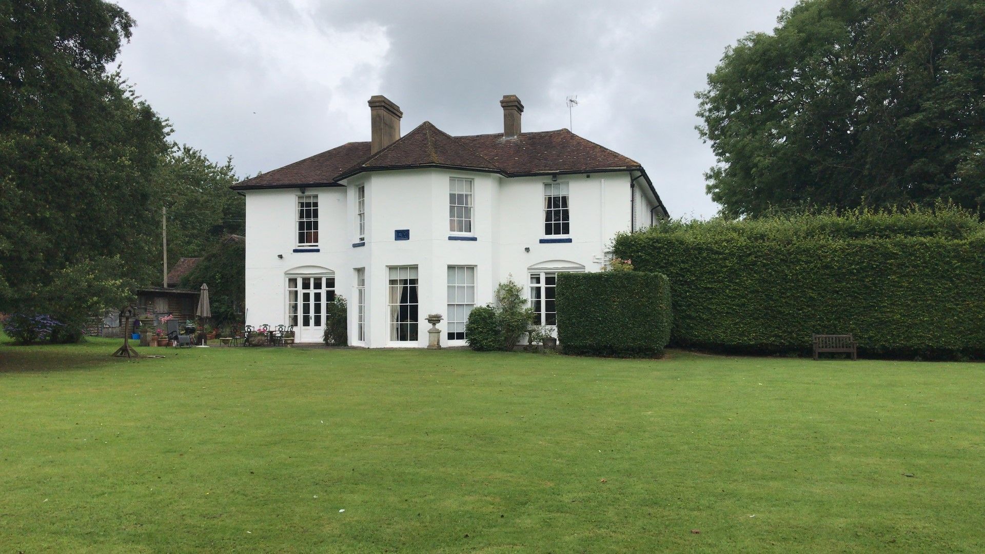 White house with large green lawn and trees under cloudy sky.