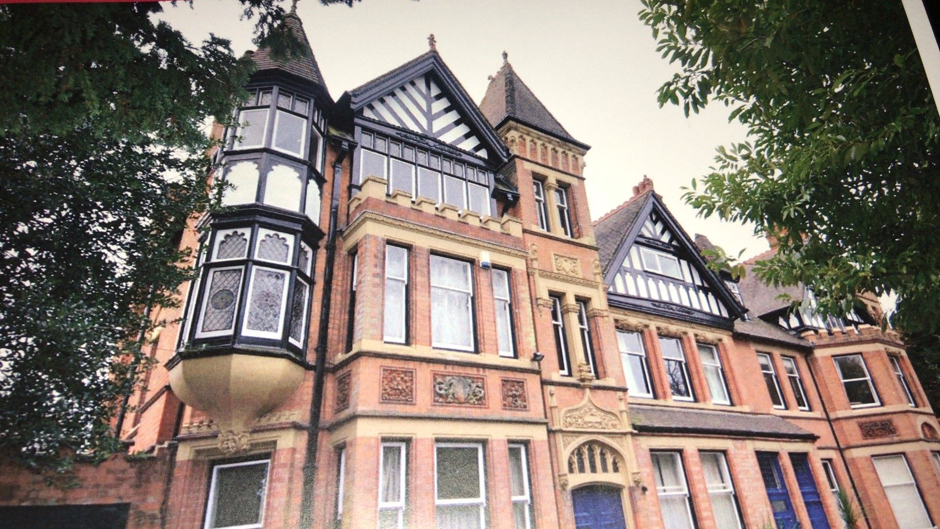 Ornate brick building with bay windows and decorative trim, trees framing the structure.