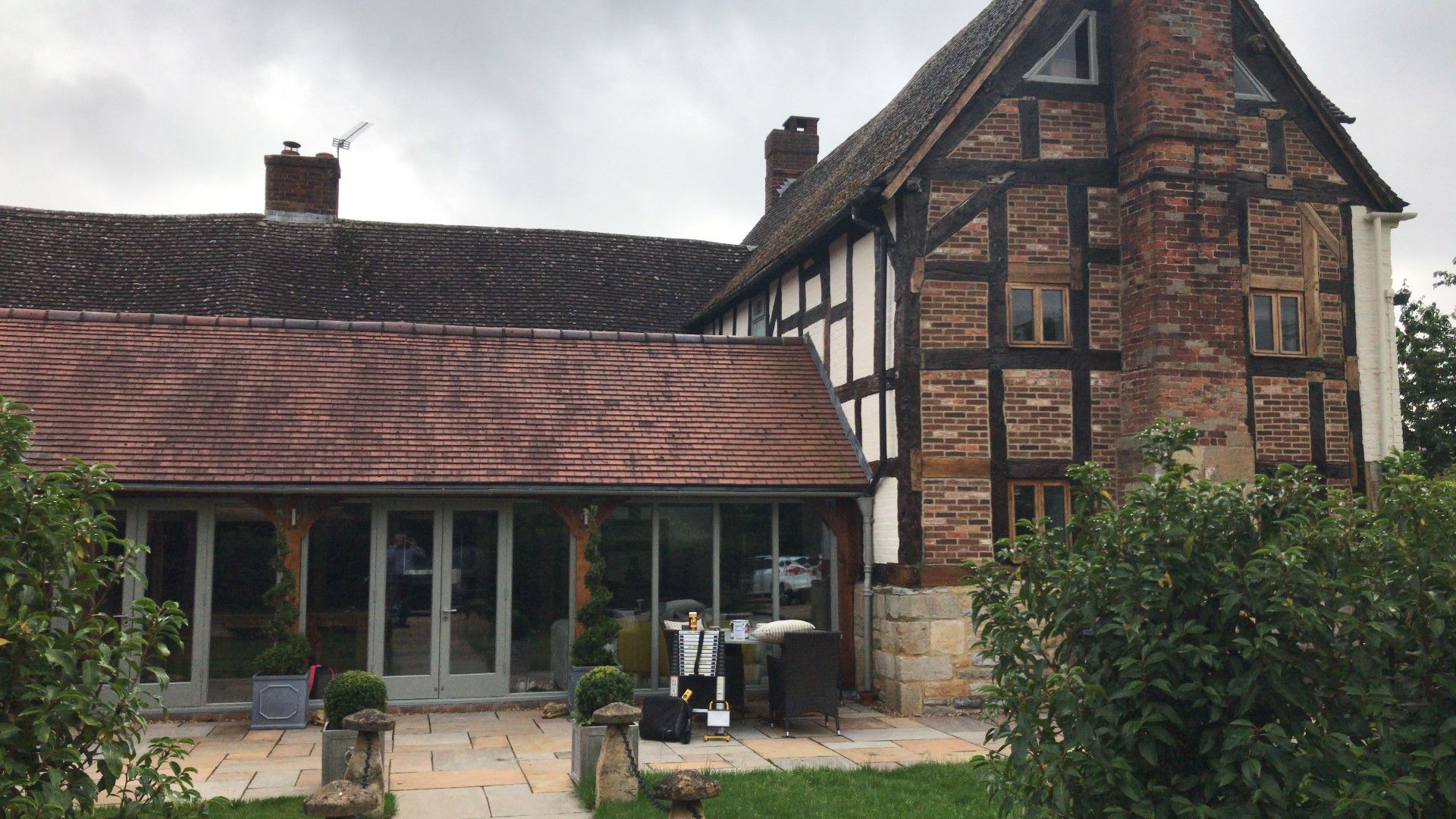 Tudor-style house with black timbers and brickwork, a glass-walled extension, and a tiled roof.