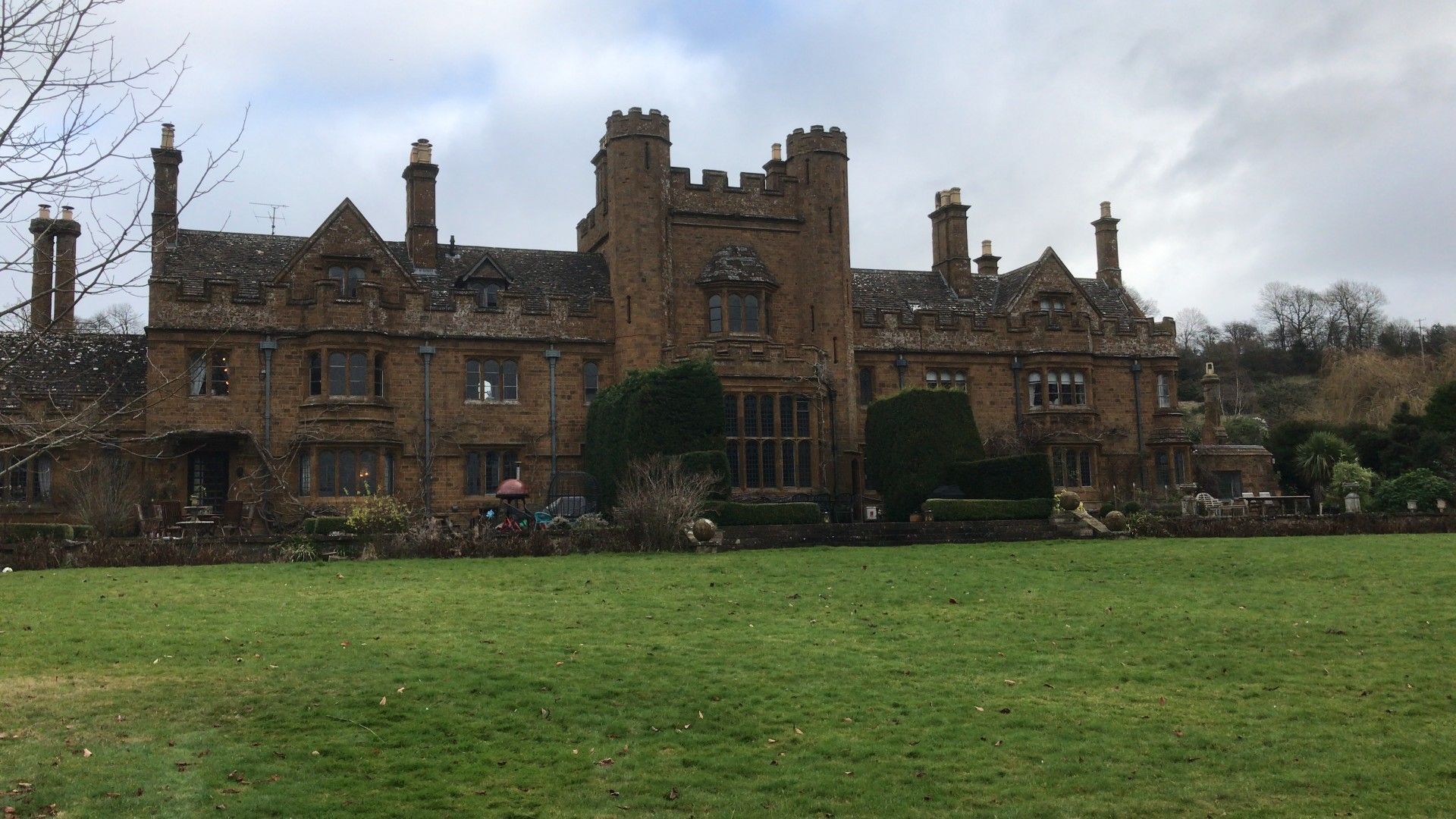 Large brown manor house with a green lawn. Overcast sky.