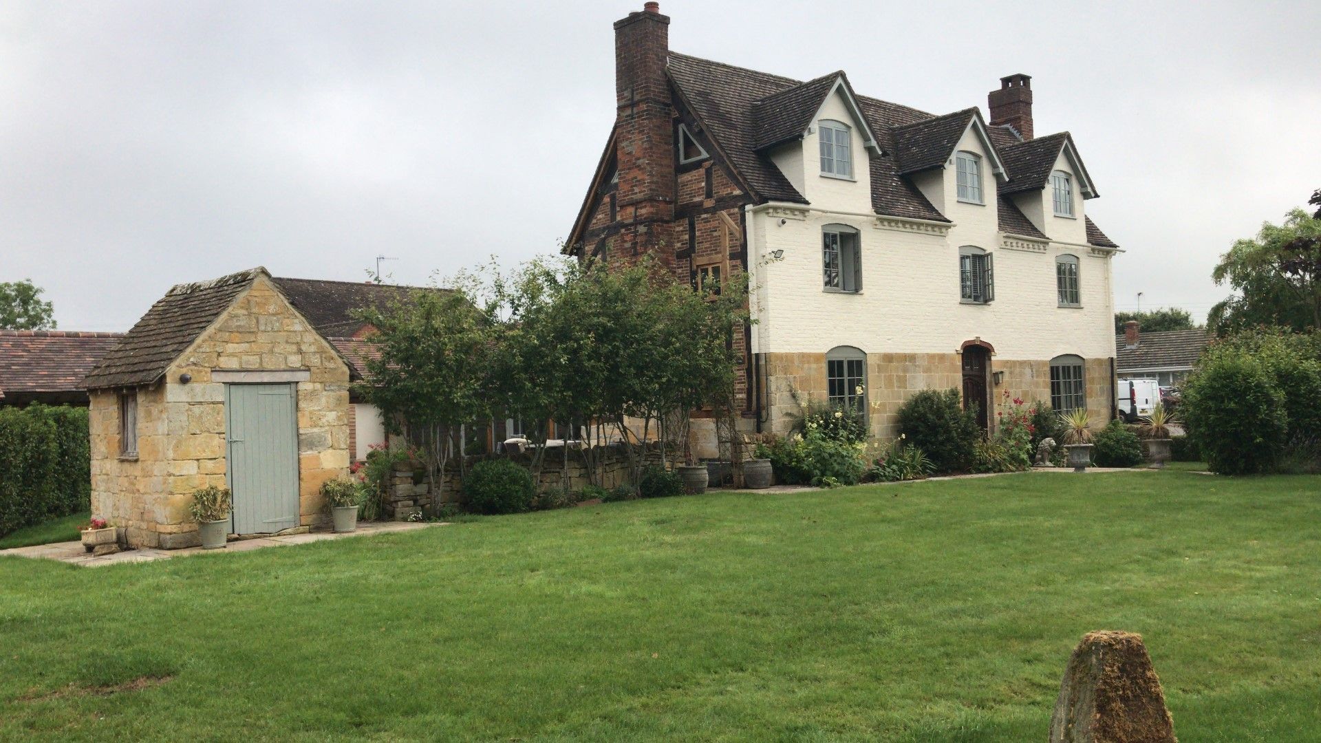 Stone cottage with attached shed and a green lawn under an overcast sky.