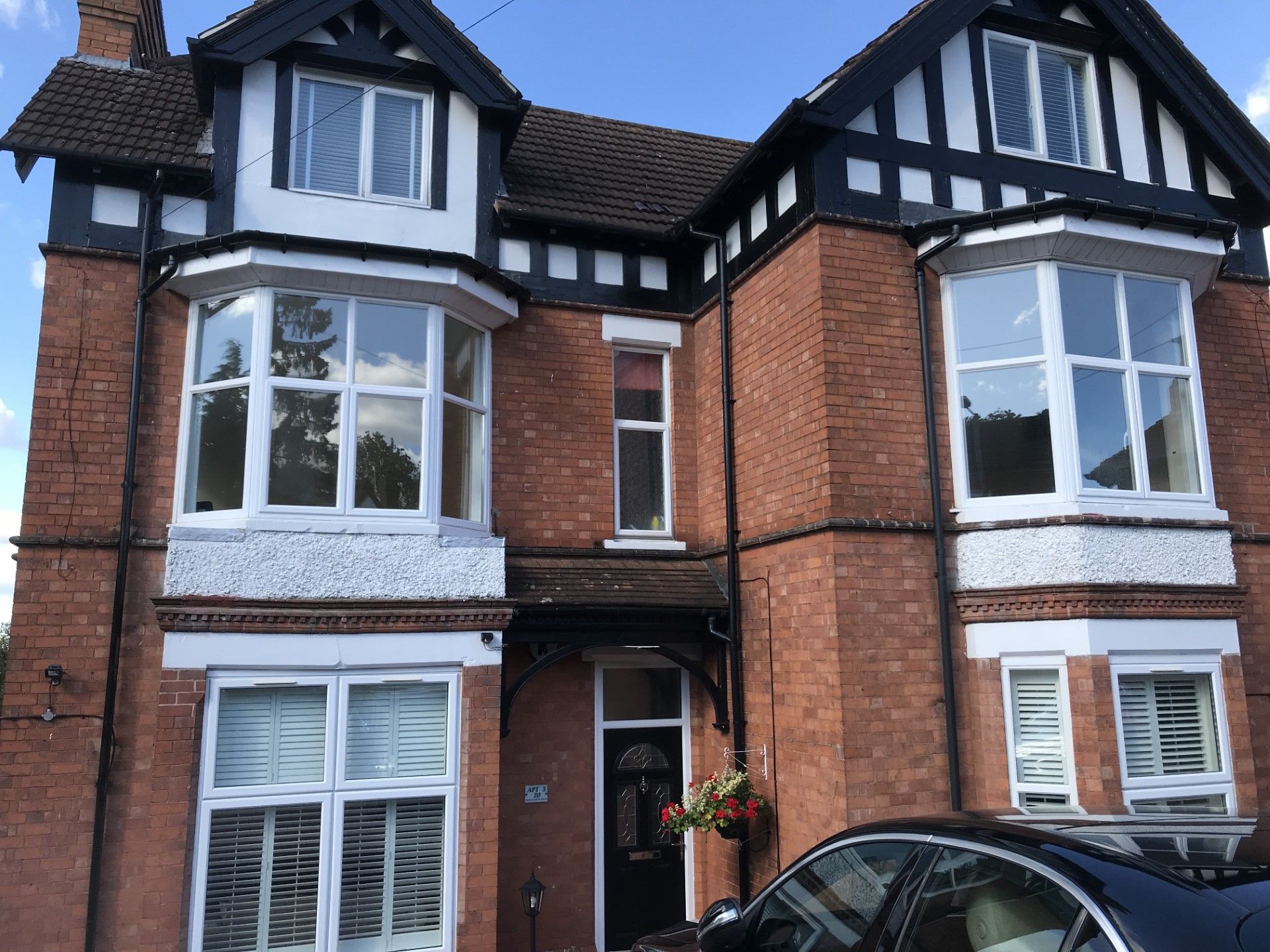 Two-story brick house with black trim and large bay windows. A car is parked in front.