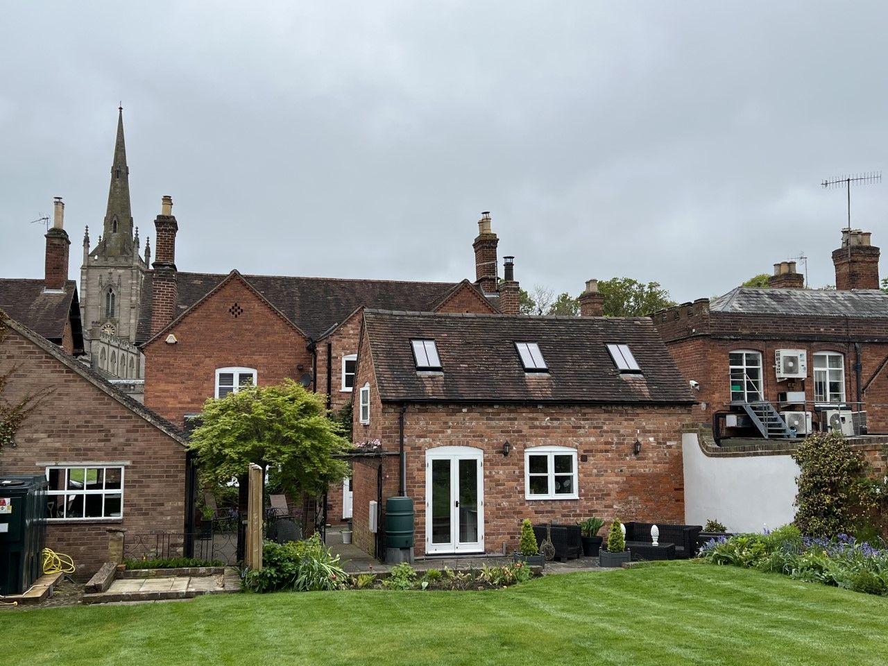 Brick buildings and a church steeple against an overcast sky, with a grassy lawn in the foreground.