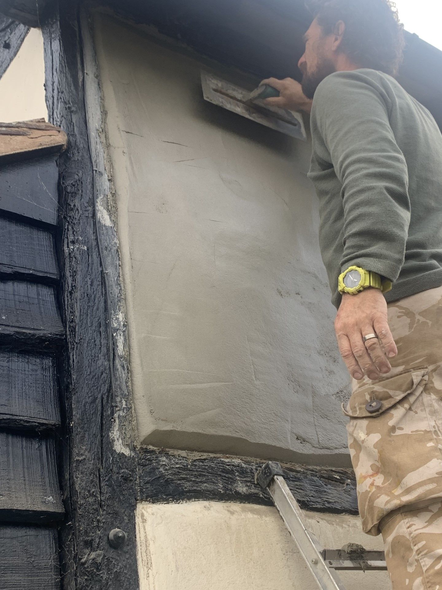 Man applying plaster to a building's wall with a trowel outdoors.