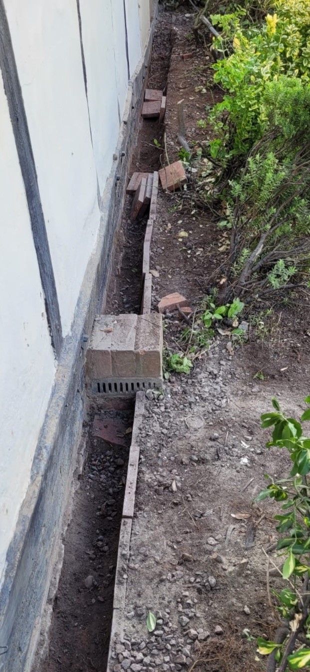 Trench with brick and concrete along a wall, possibly a drainage system.