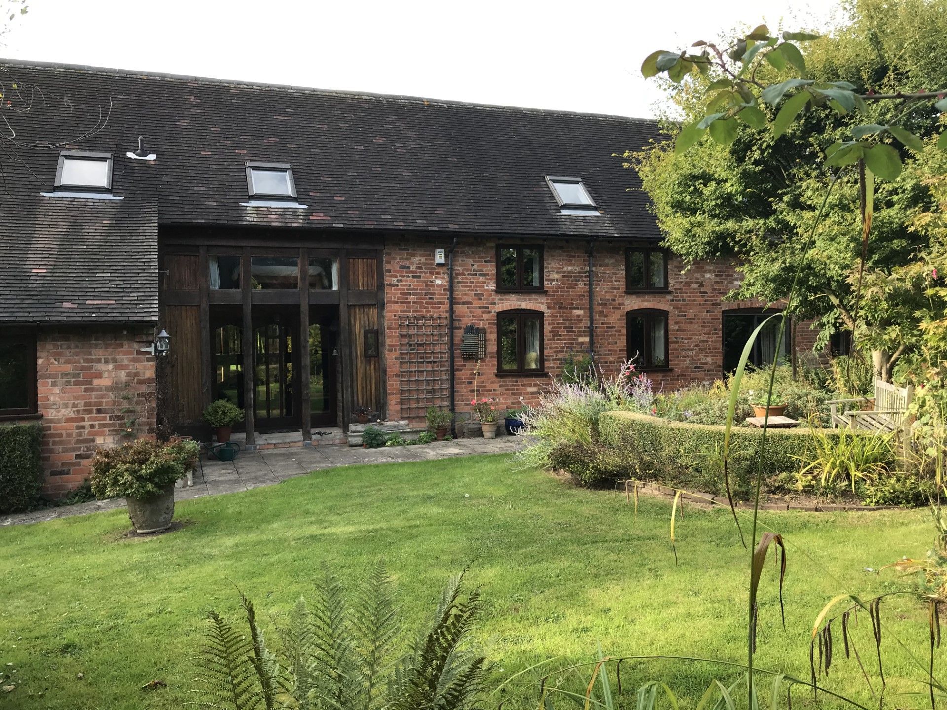 Brick building with glass doors, set in a grassy yard with a garden.