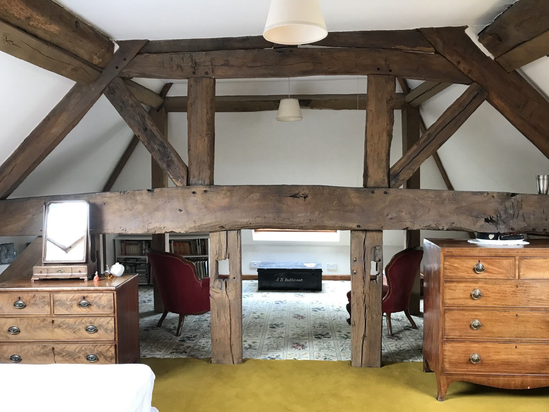 Bedroom with exposed wooden beams, two chests, two red chairs, and a rug.