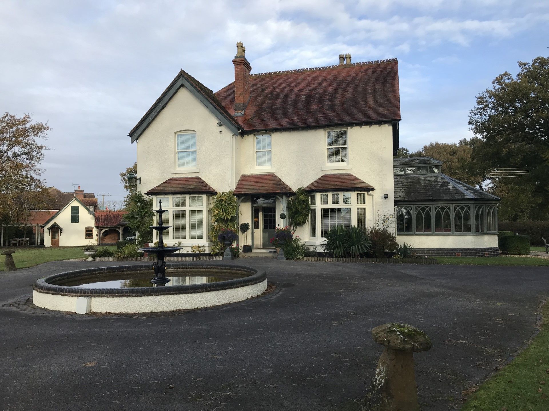 Cream-colored house with red roof, fountain in the foreground, and a clear sky.