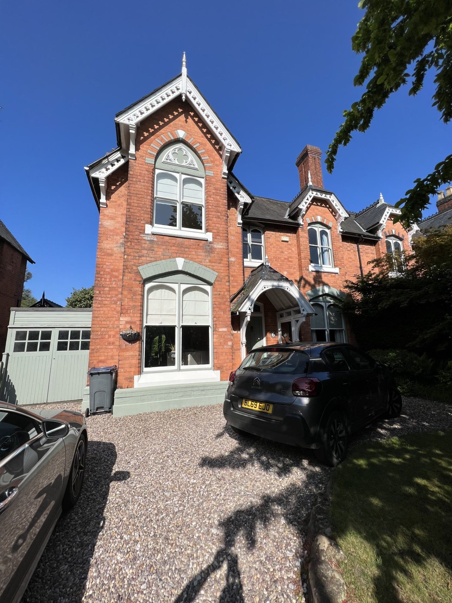 Red brick house with gray gravel driveway, a black car, and a car without a front, under blue sky.