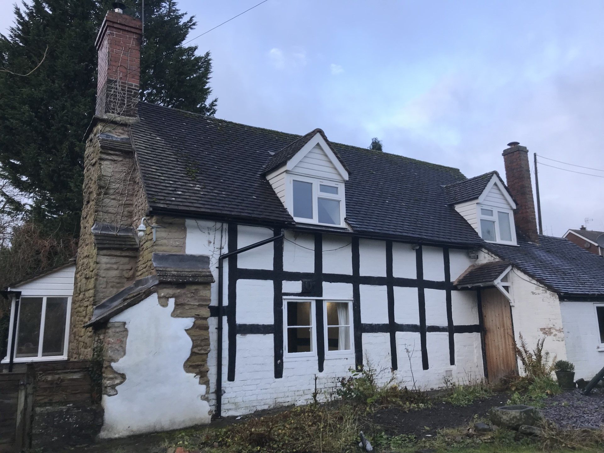 Cottage with black timber framing on white walls, dark roof, brick chimney, and small additions.