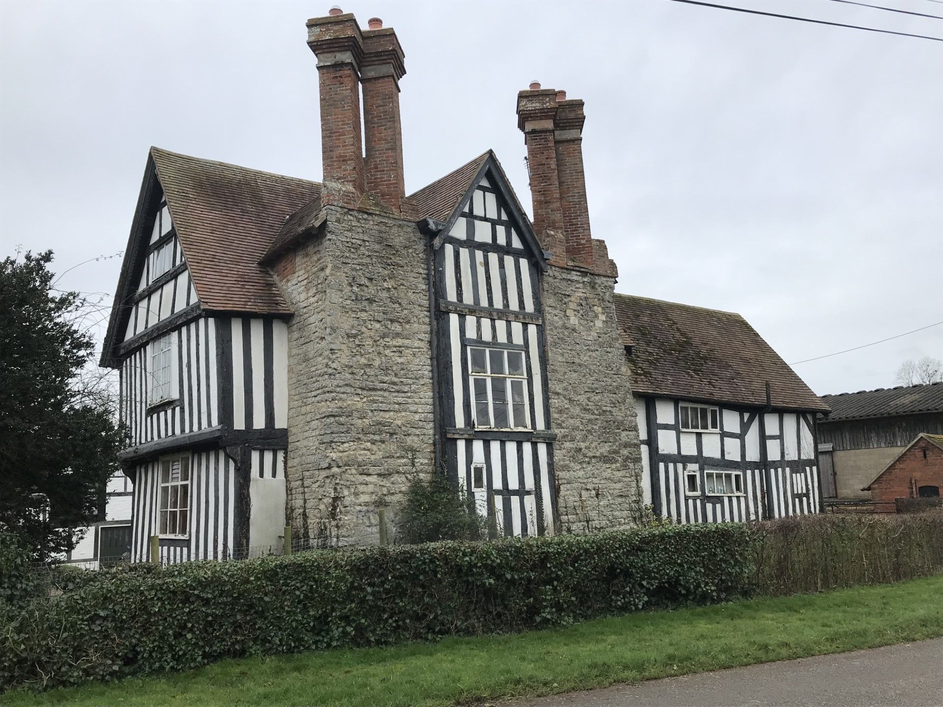 Half-timbered Tudor house with black and white beams, stone walls, and red-tiled roof.