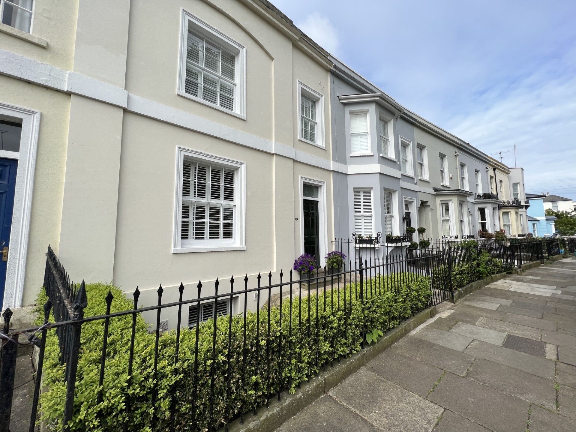 Row of townhouses with light-colored exteriors, black iron fence, and sidewalk under a blue sky.