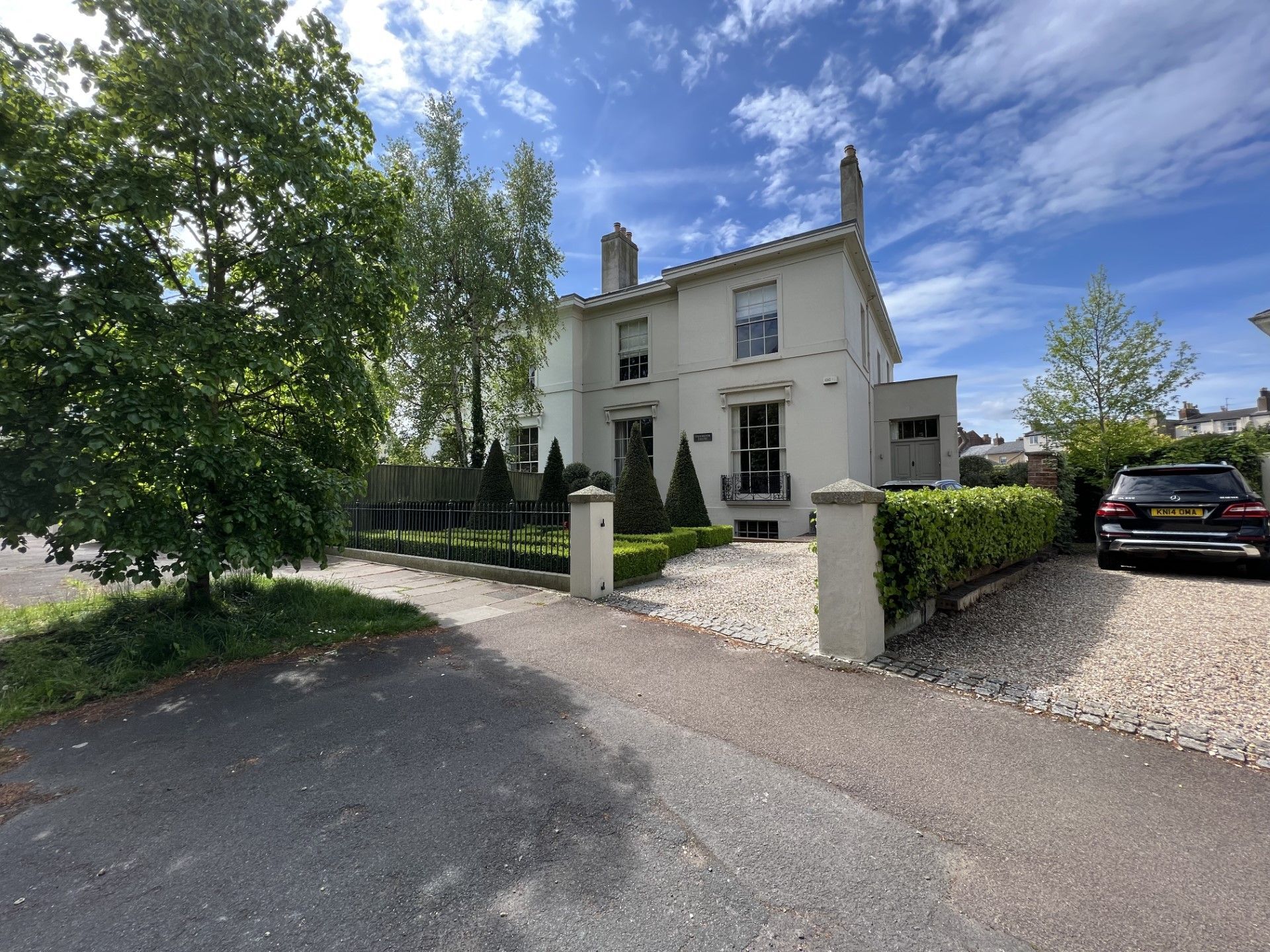 White house with gravel driveway, green hedges, and blue sky.