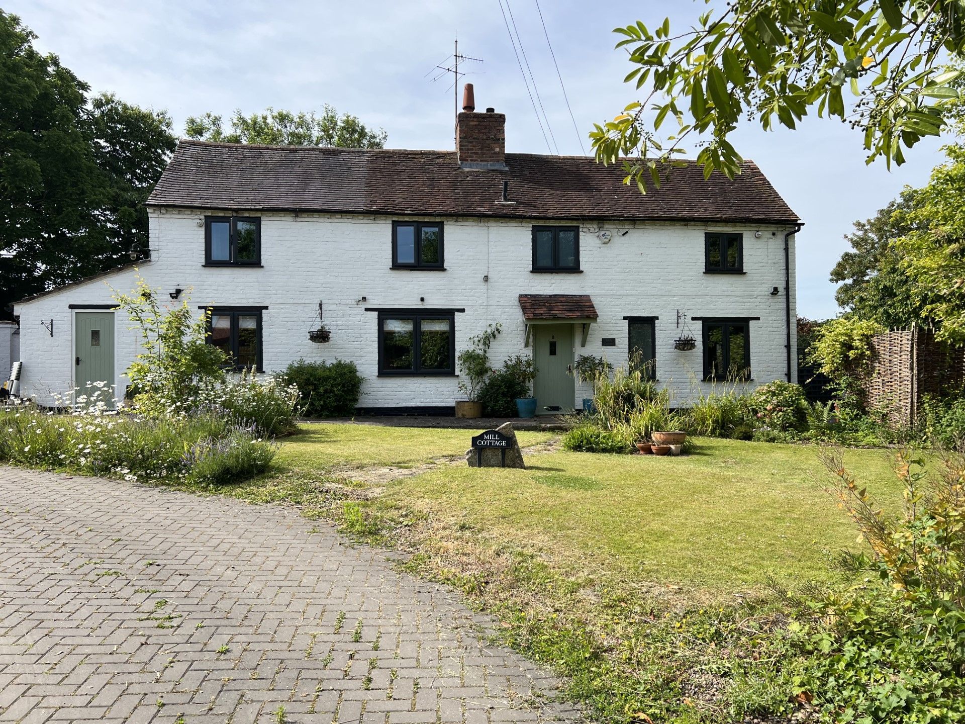 White two-story house with black windows and a light green front door; a brick driveway and grassy yard.