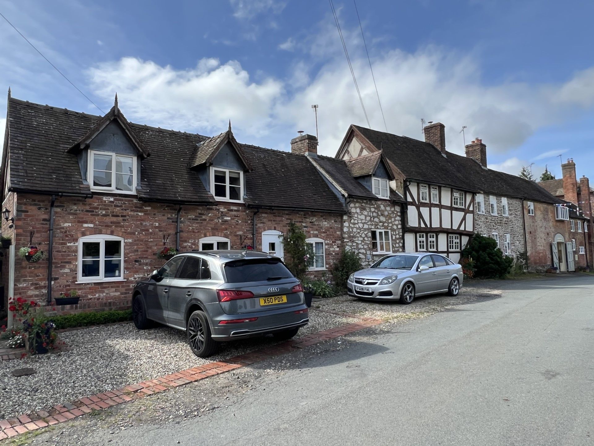Row of historic brick and half-timbered buildings with cars parked in front; blue sky overhead.