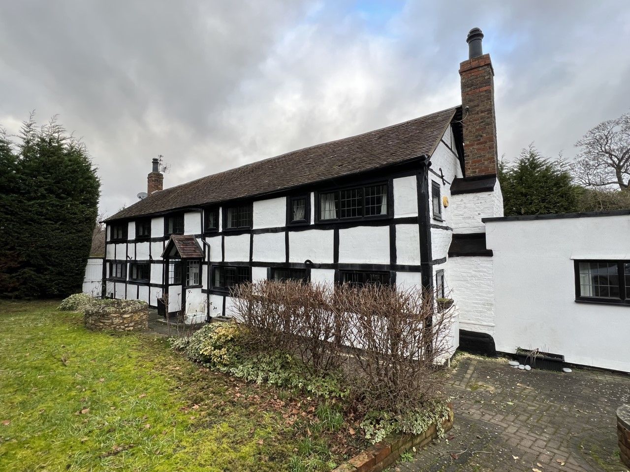 Black and white timber-framed cottage with a brick chimney under a cloudy sky.