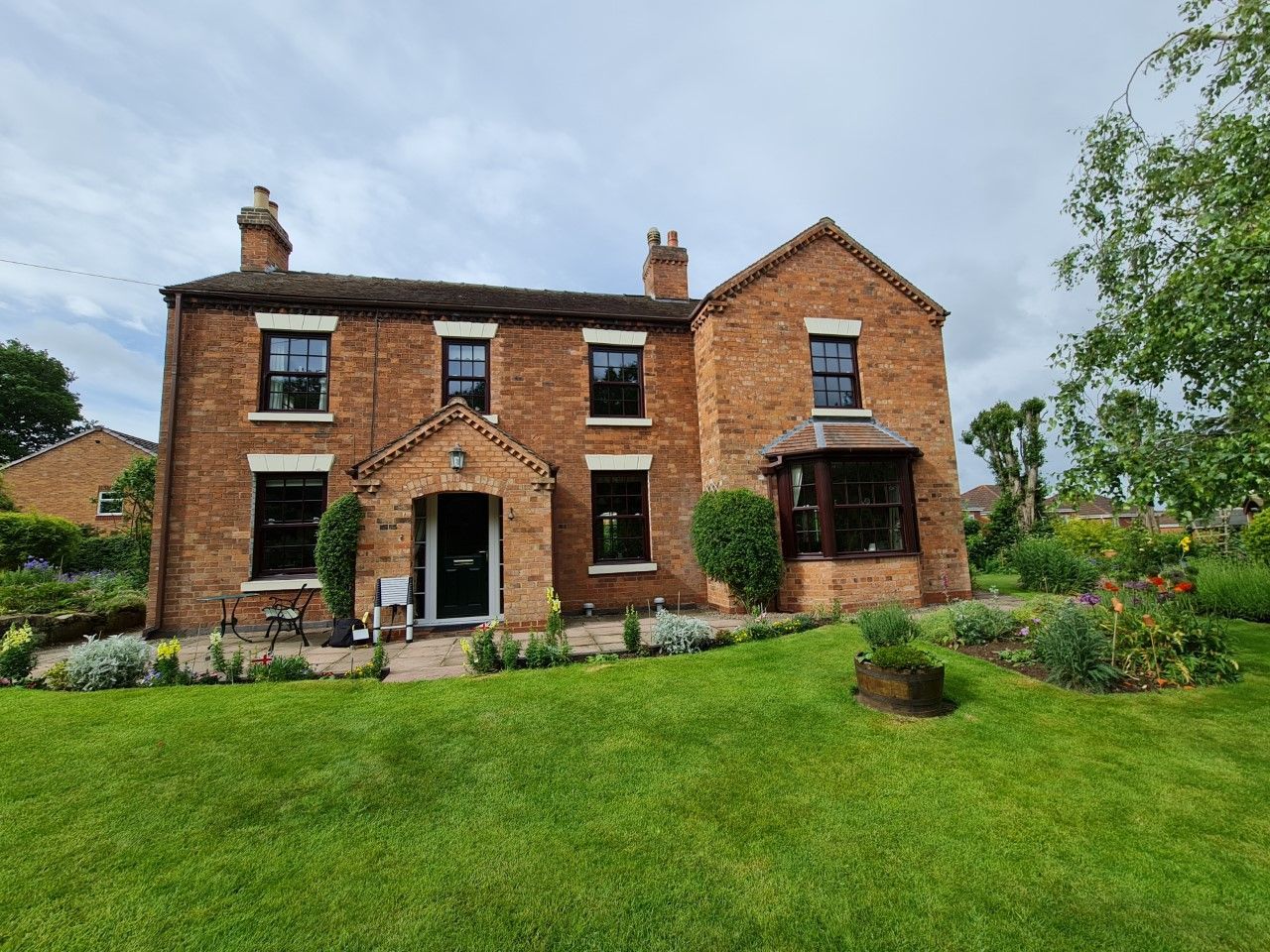 Brick house with green lawn, front garden. Black windows, door. Cloudy sky.