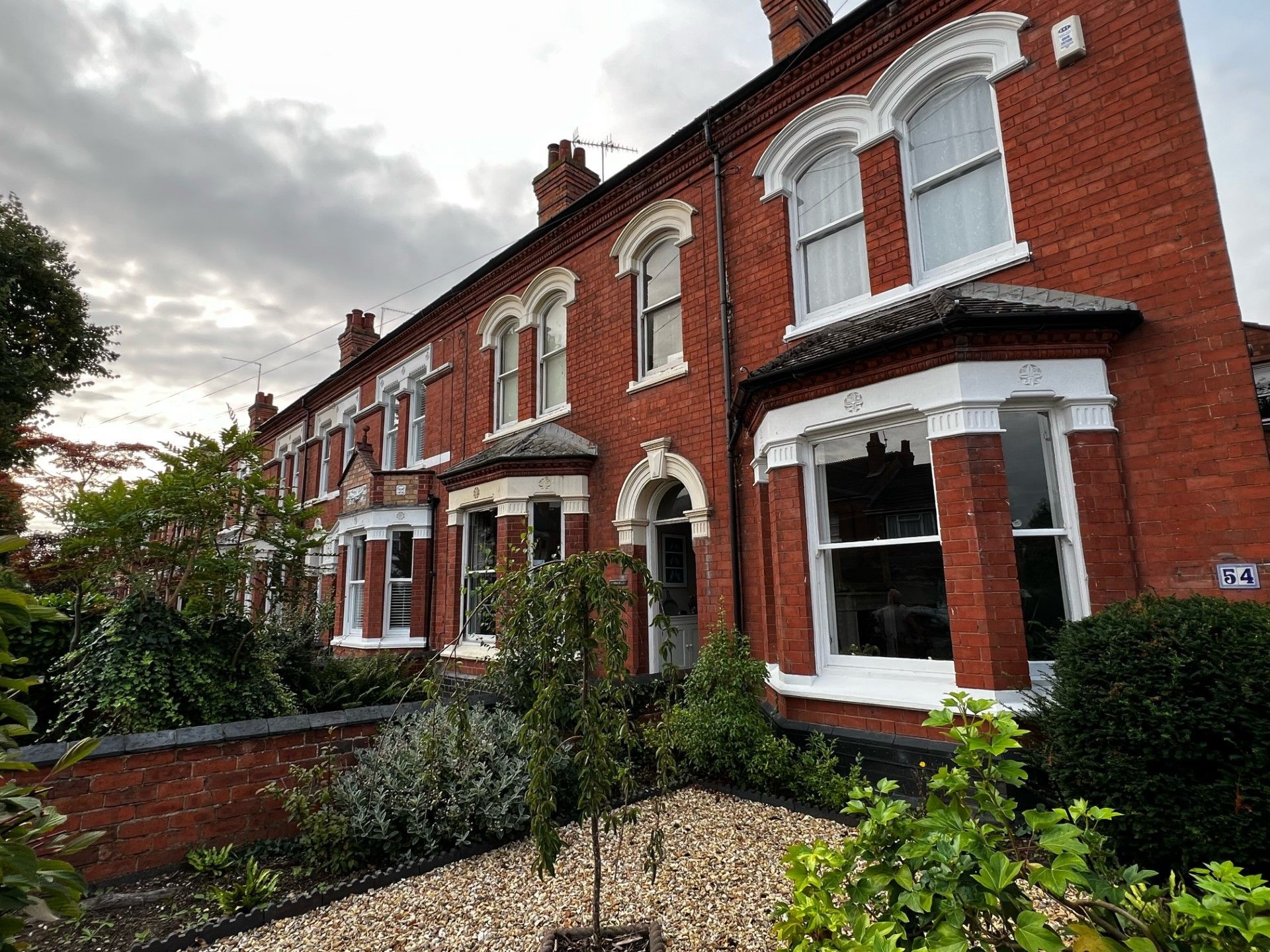 Row of red brick Victorian houses with white window frames and cloudy sky.