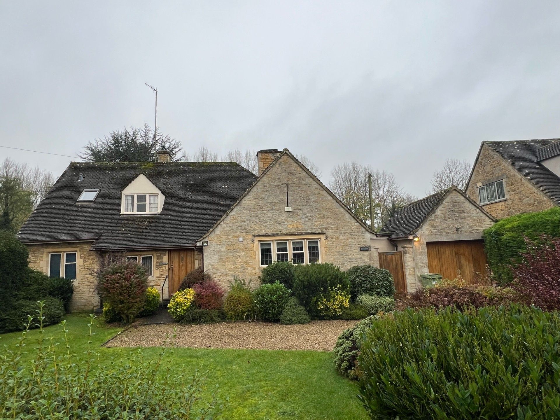 Stone cottage with thatched roof, garden with shrubs and lawn under cloudy sky.