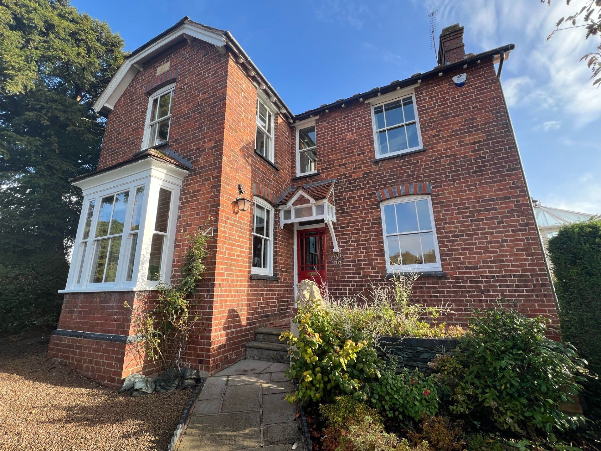 Red brick house with white-framed windows and a red front door on a sunny day.