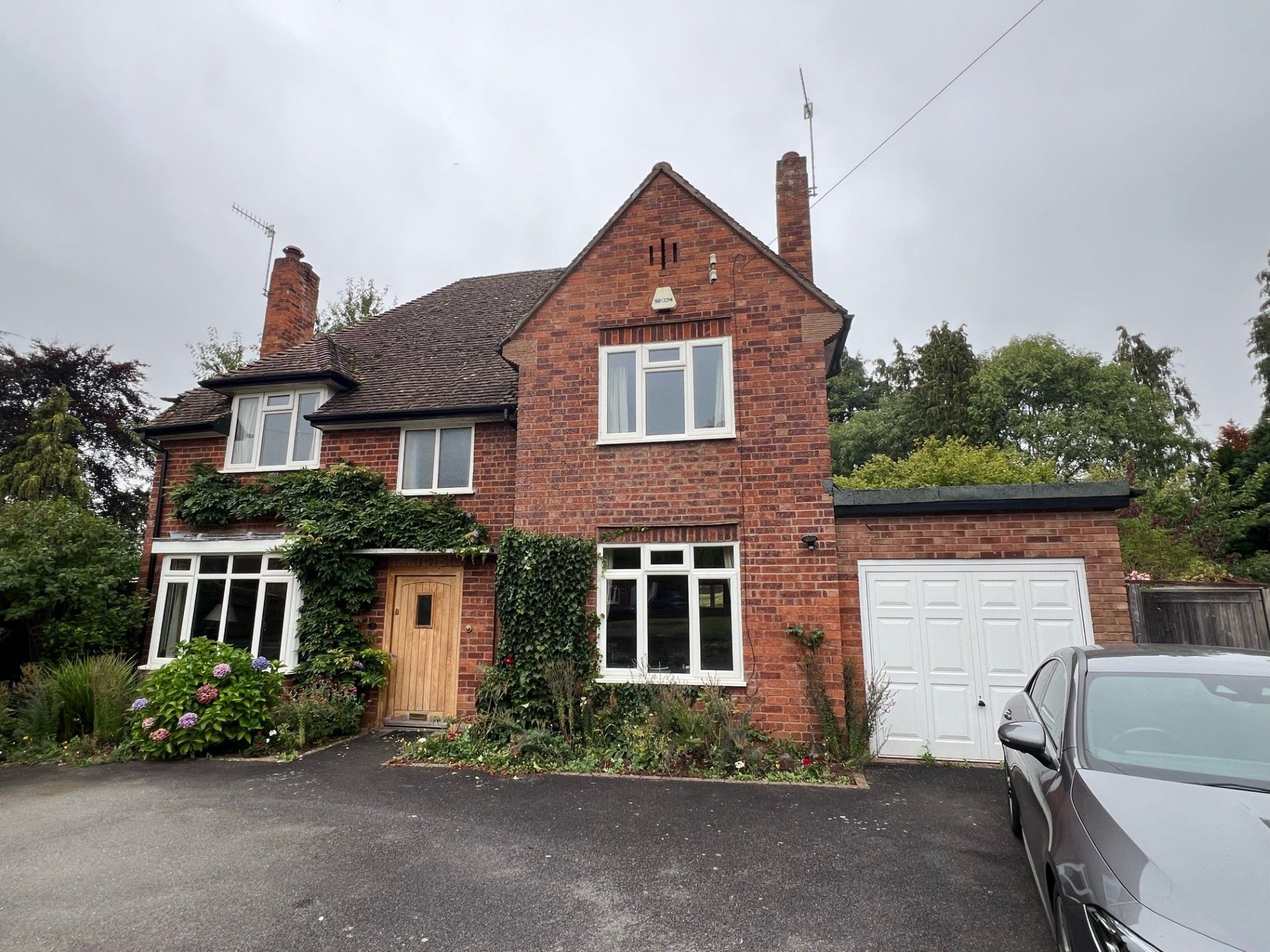Red brick house with white-framed windows, ivy, a wooden door, and an attached garage; car parked in driveway.