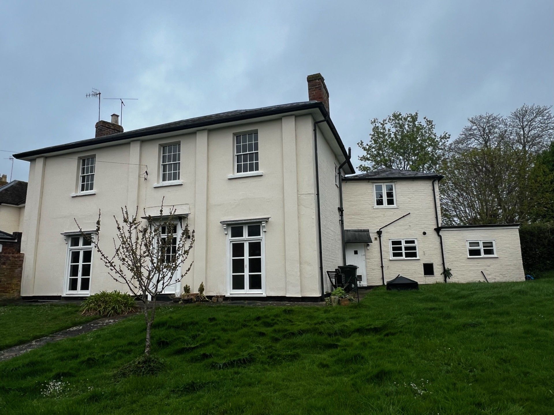 White house with black roof, set on a grassy hill under a cloudy sky.