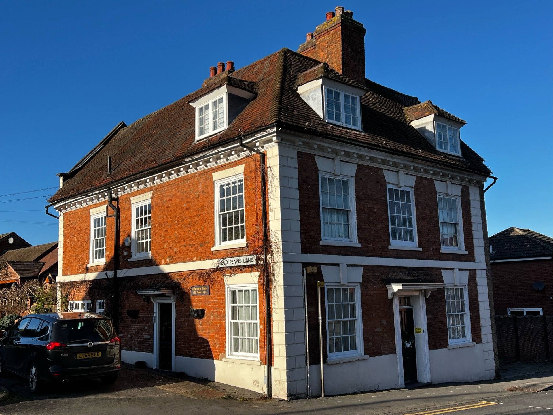 Brick building with white trim, three floors, dormers, and a car parked nearby.