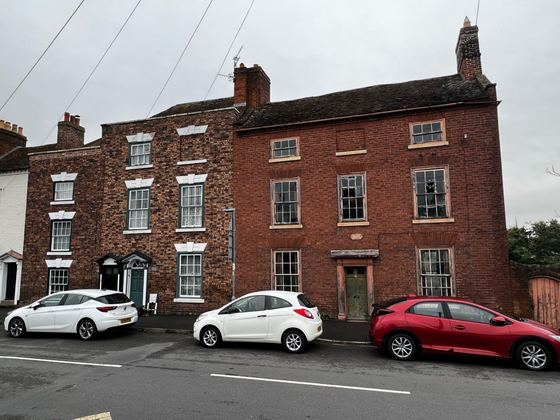 Red brick building with white cars parked in front, cloudy sky.