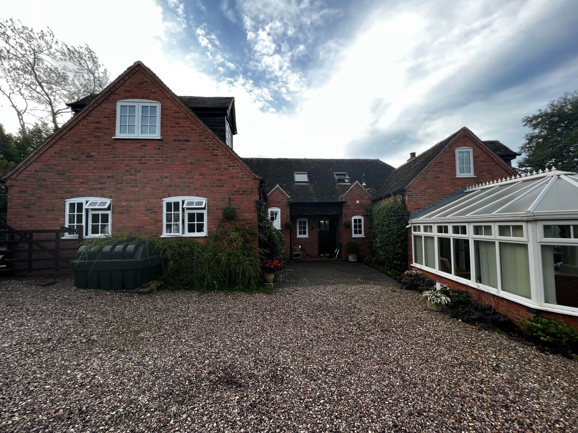 Brick house with white window frames, gravel driveway, and a conservatory.