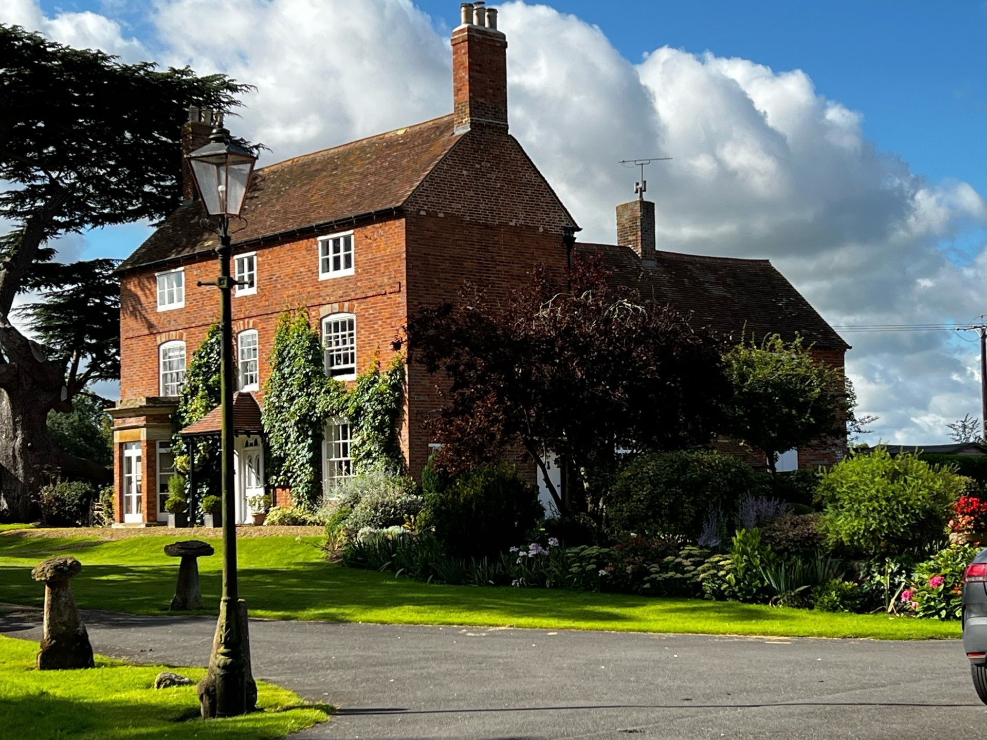 Brick house with red roof, greenery, street lamp, and blue sky.