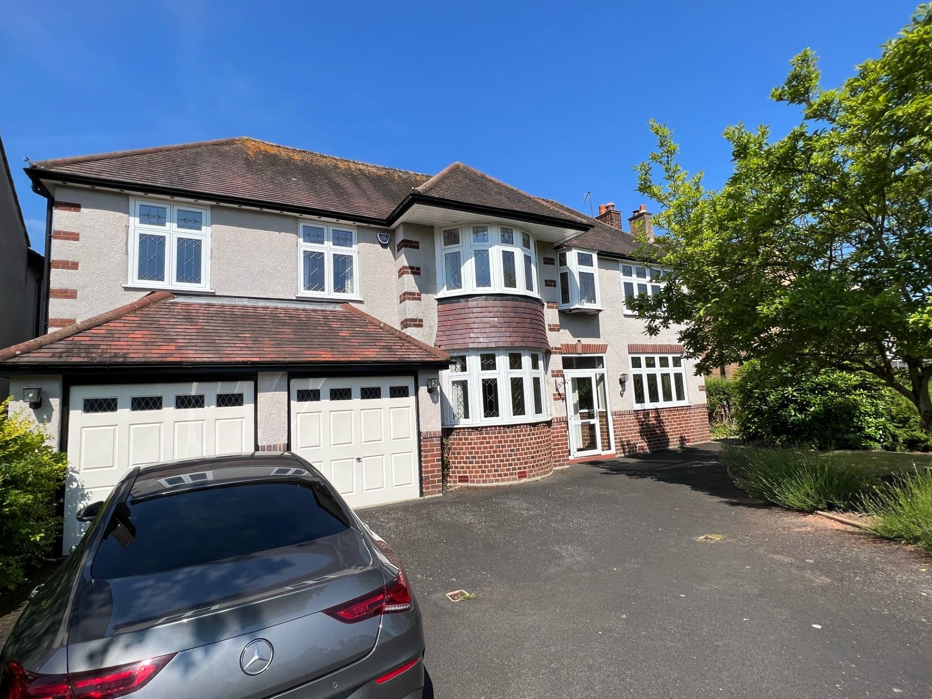 Two-story house with red brick, bay windows, and a two-car garage. A gray car is parked in the driveway.