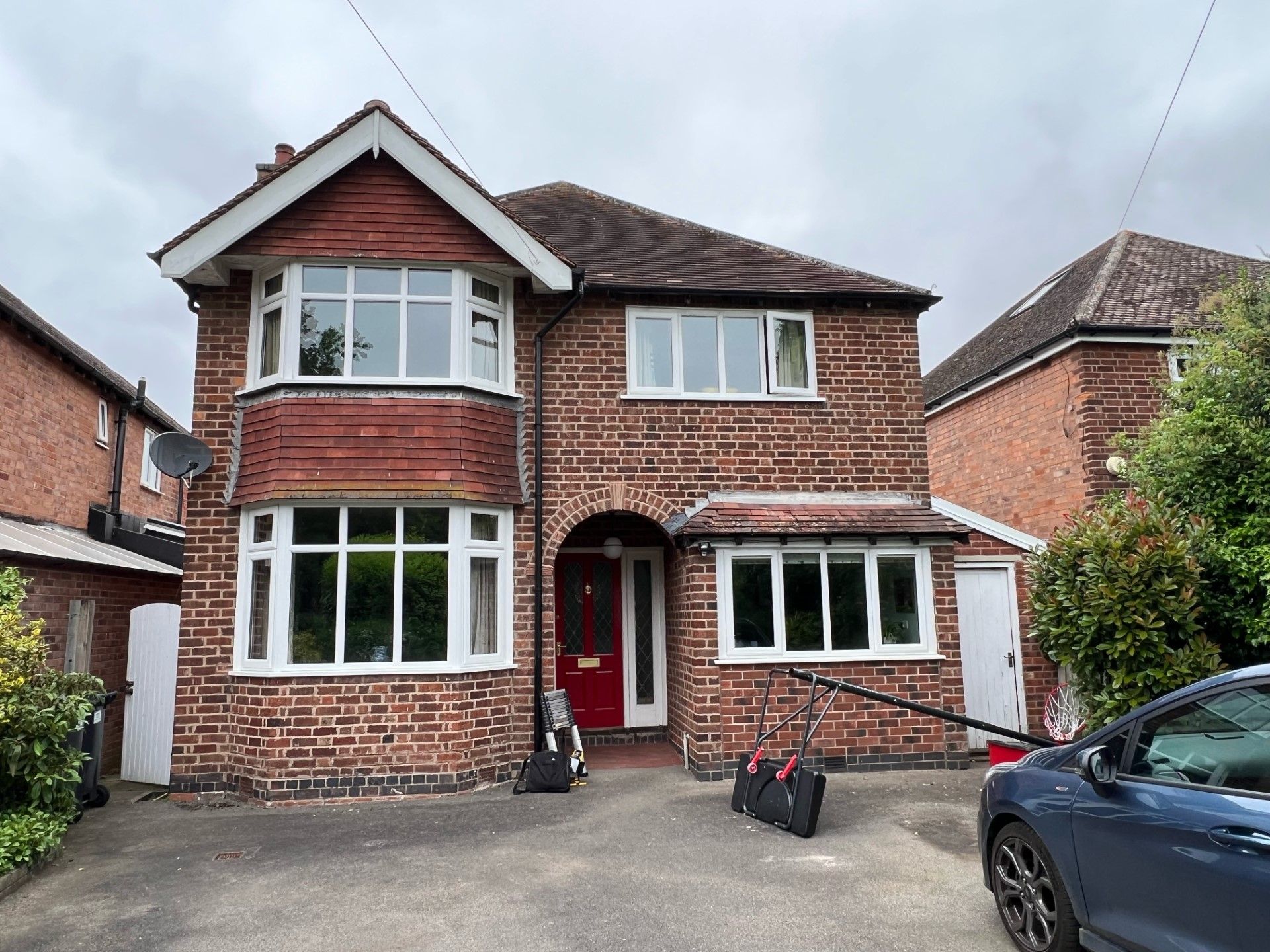 Two-story brick house with bay windows and a red front door. A dark car is parked in front.