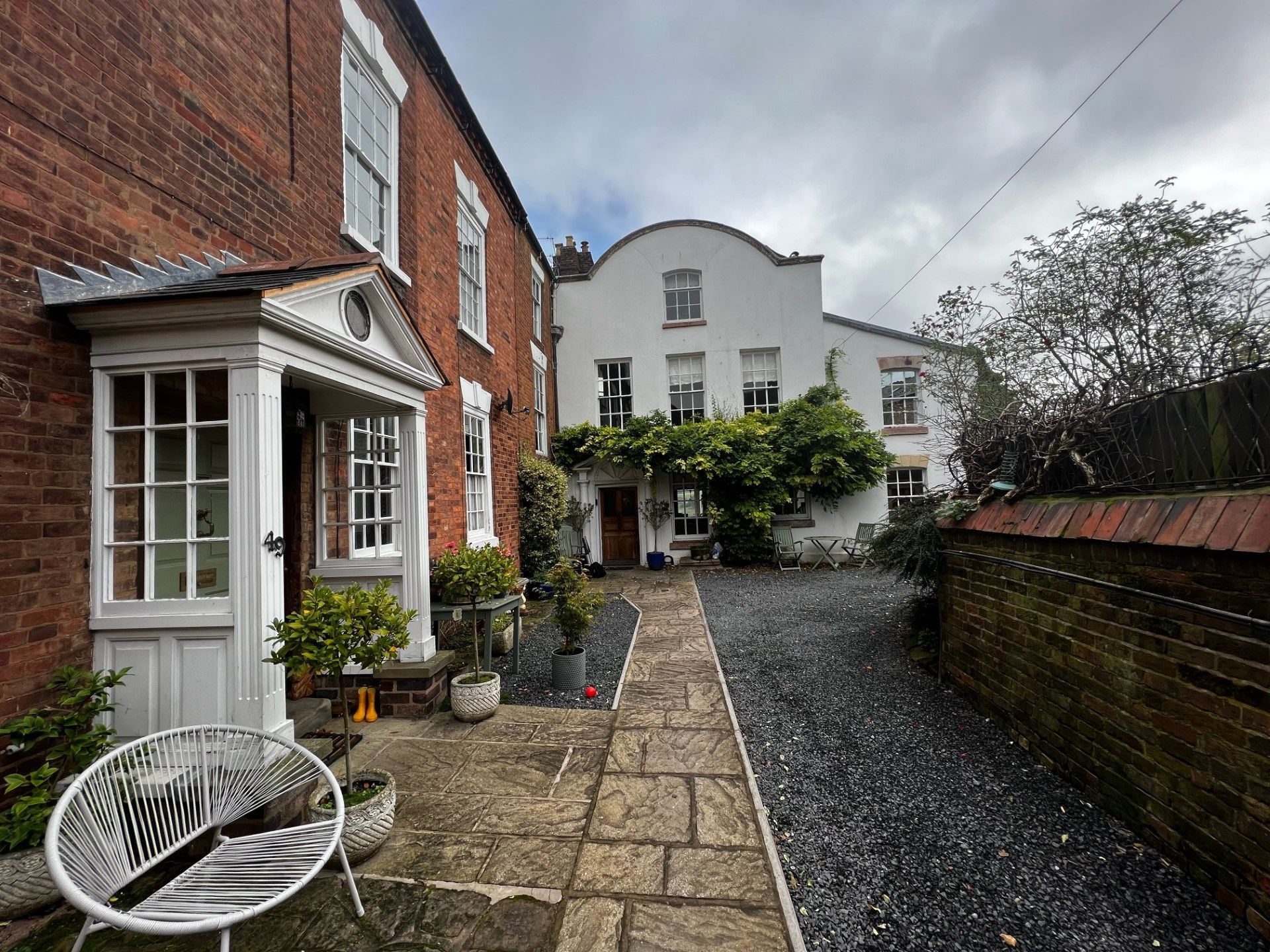 Brick and white buildings with a stone pathway leading to a doorway, cloudy sky overhead.