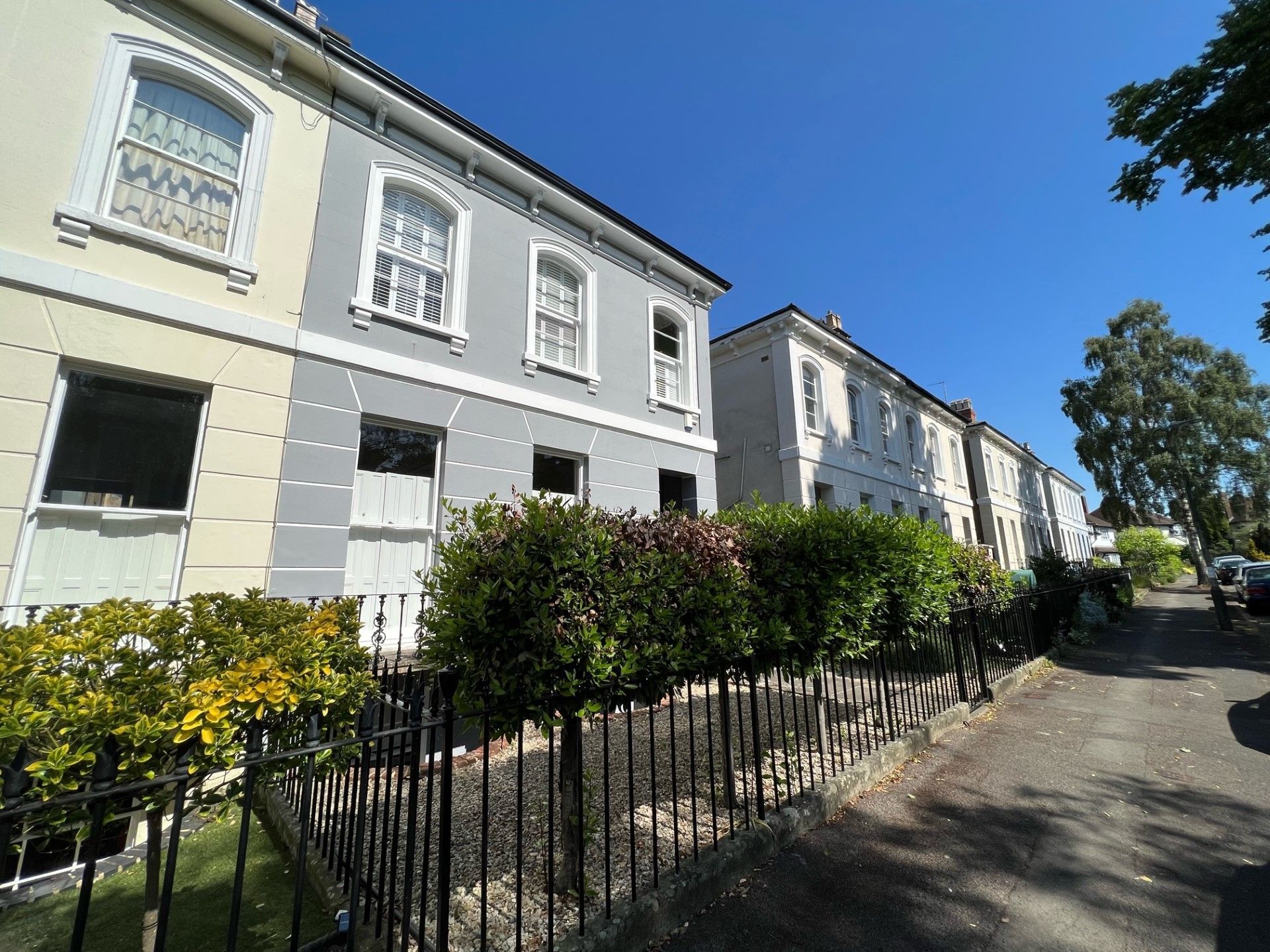 Row of townhouses, painted light gray, with black railings and a sunny blue sky.