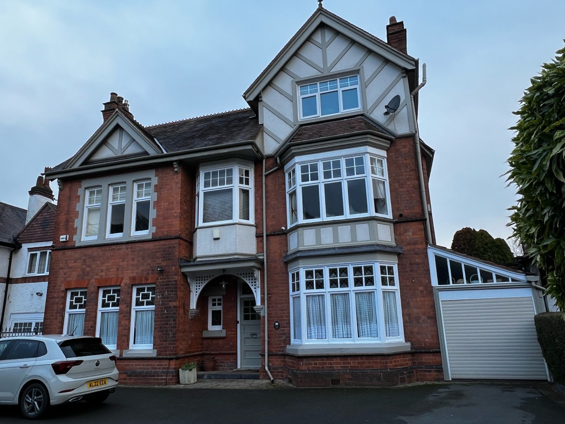 Red brick house with white trim and multiple windows, driveway with a car, and a garage.