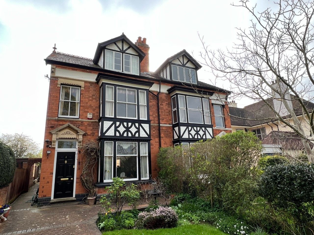 Red brick house with black trim, bay windows, and a garden.