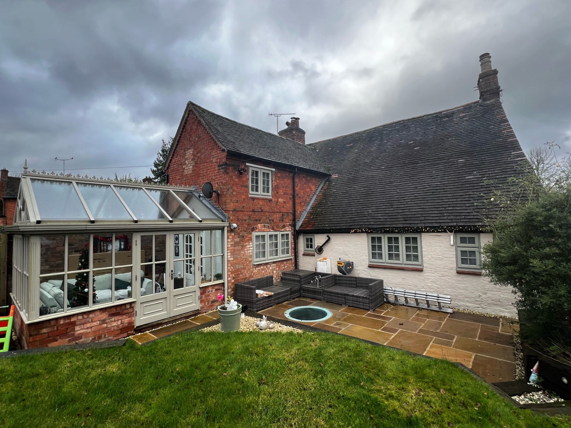 Red brick house with a sunroom, patio, and overcast sky.