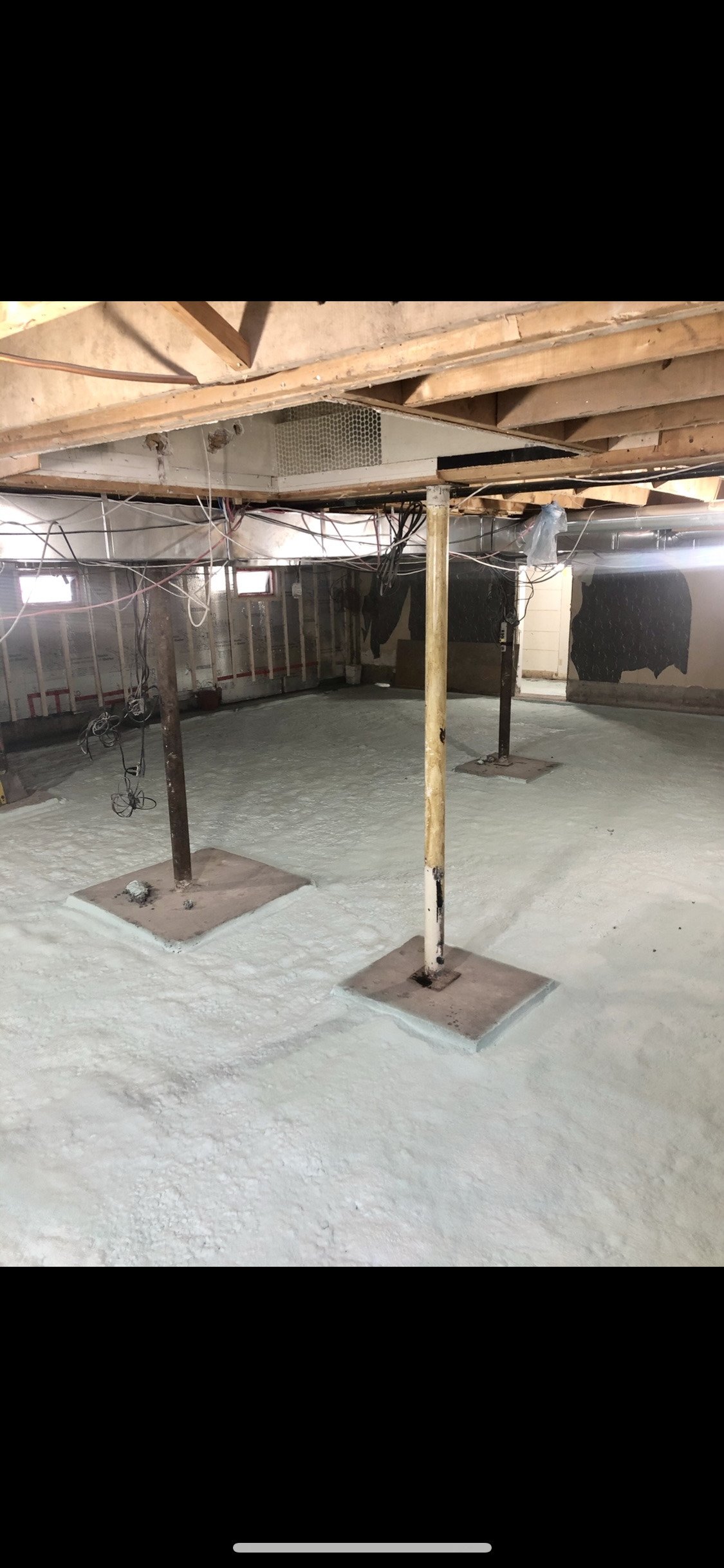 Sous-sol intérieur avec colonnes de soutien soutenant des poutres en bois. Sol et murs peints en gris.