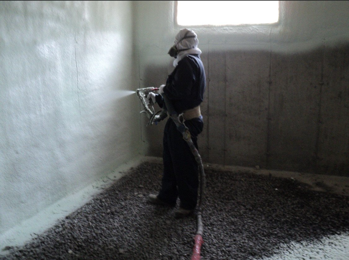 un homme pulvérise de la mousse sur un mur dans une pièce.