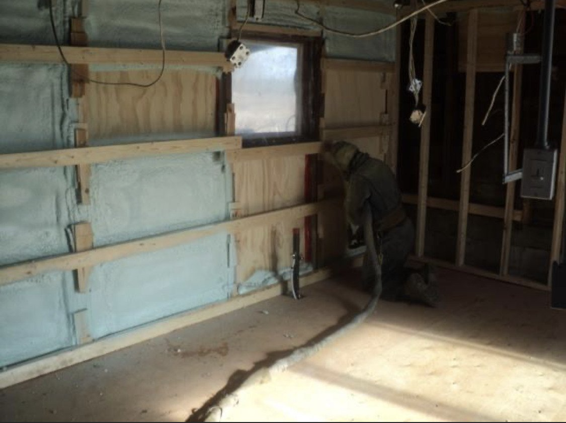 un homme pulvérise de l isolant sur un mur dans une pièce