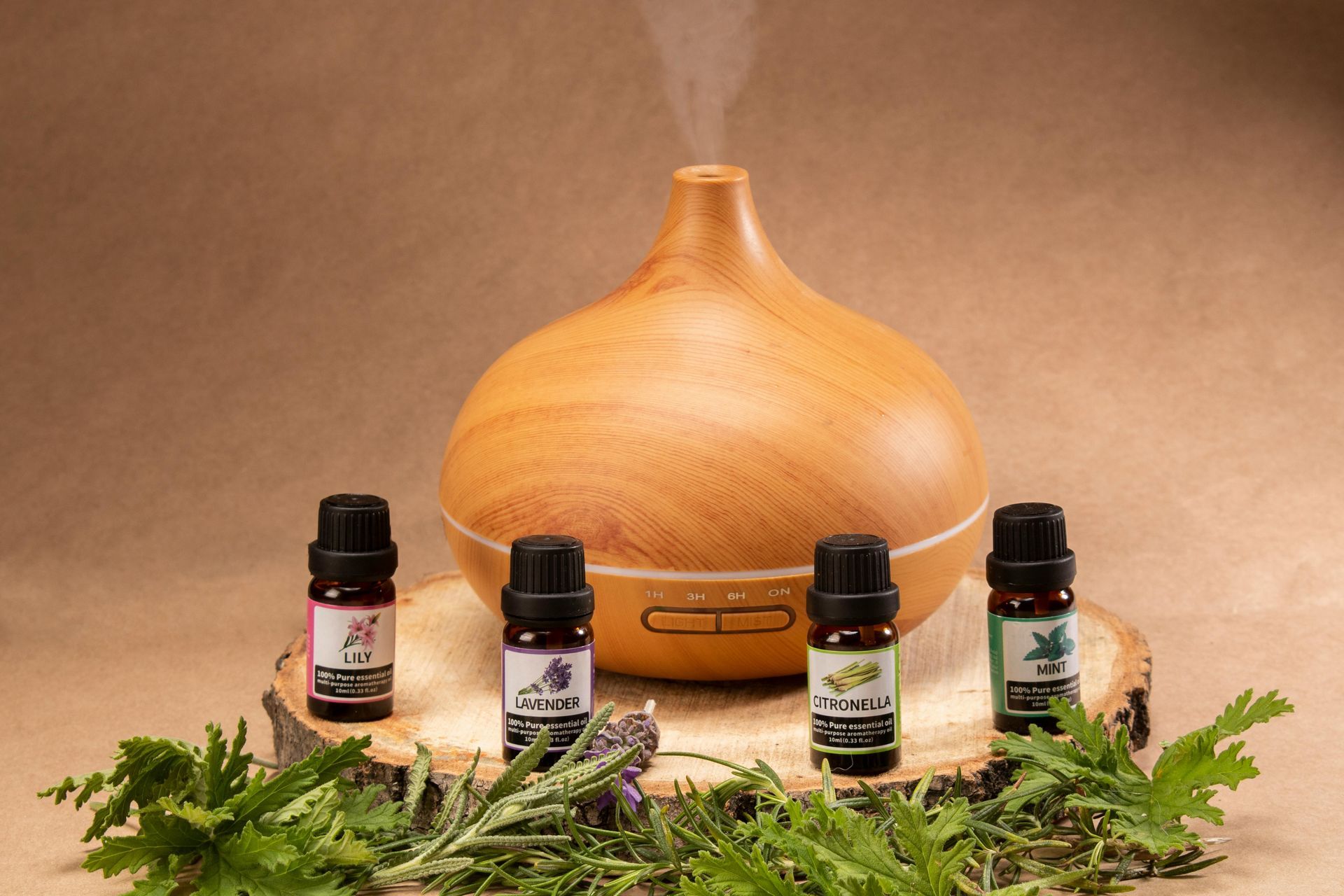Un diffusore in legno con quattro piccole boccette di oli essenziali su un vassoio, circondato da erbe aromatiche verdi.