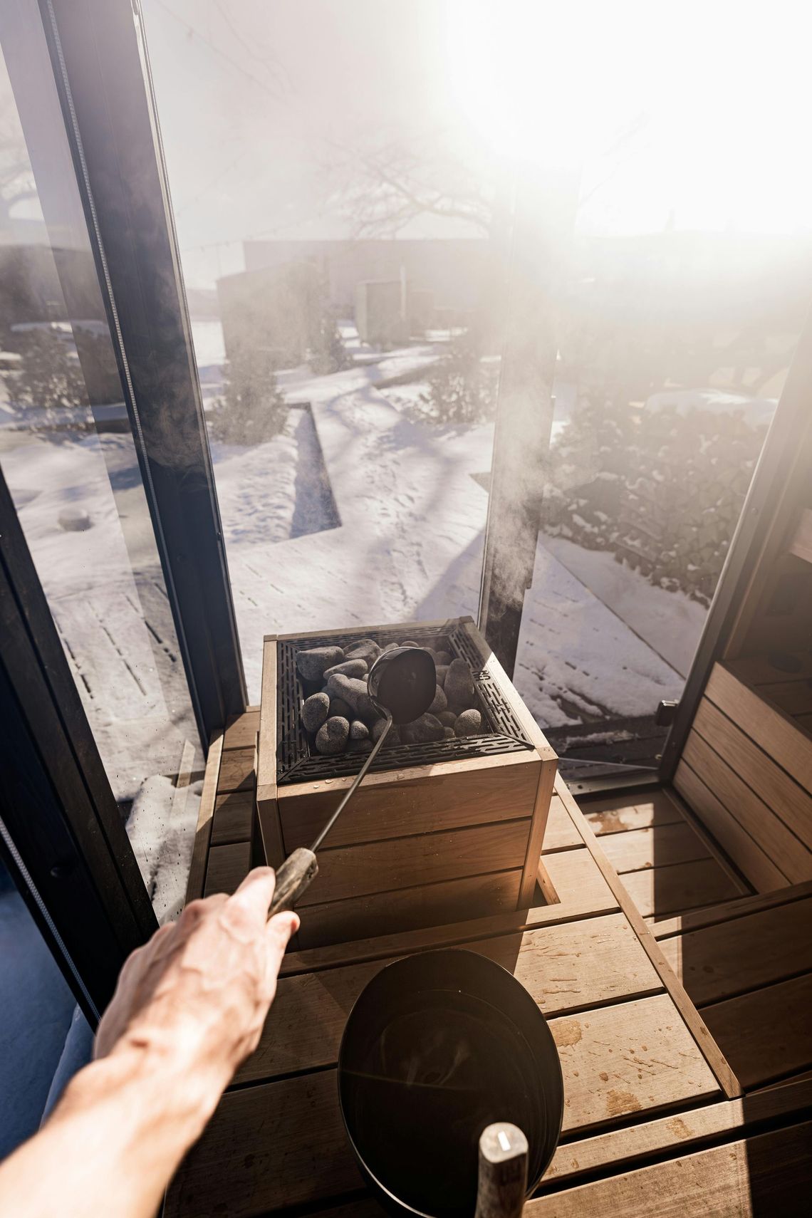 Balcone soleggiato con neve all'esterno, una fioriera e la mano di una persona che regge un palo in primo piano