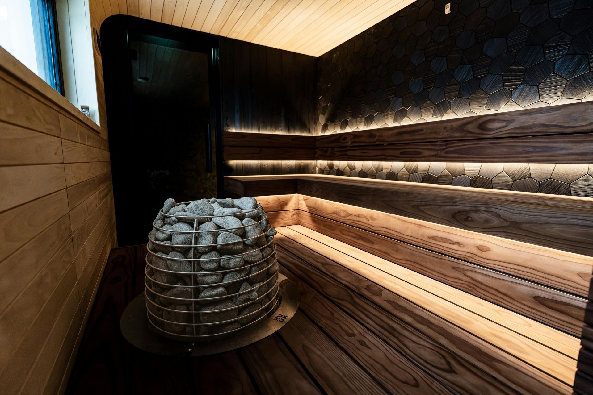Interno della sauna in legno con panche e una pila di pietre accanto alla stufa.